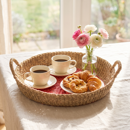 Woven seagrass round tray with pink centre serving coffee and pastries on a sunlit breakfast table