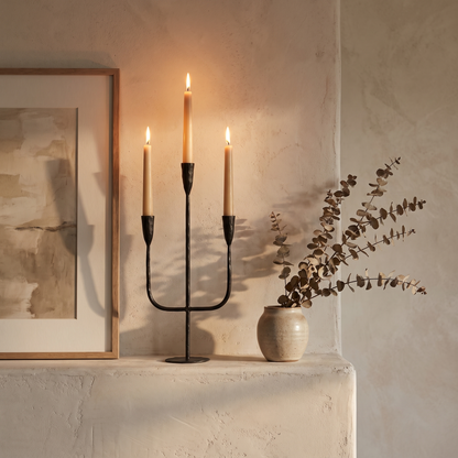 Hand-forged iron candelabra with lit tapers styled on a plaster mantelpiece