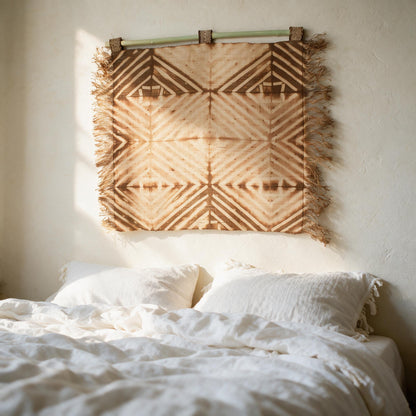 Rust raffia shibori diamond wall hanging above a bed